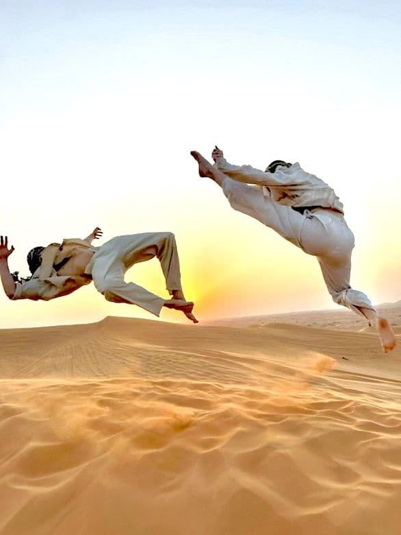 Two guests leaping on a dune crest in the golden light