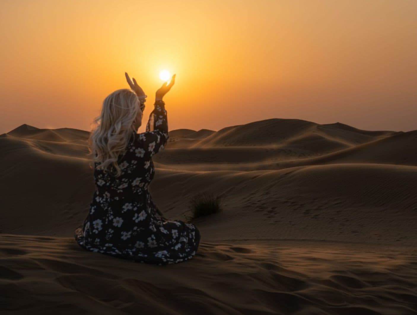 Guest raising her hands towards the low sun on a desert dune