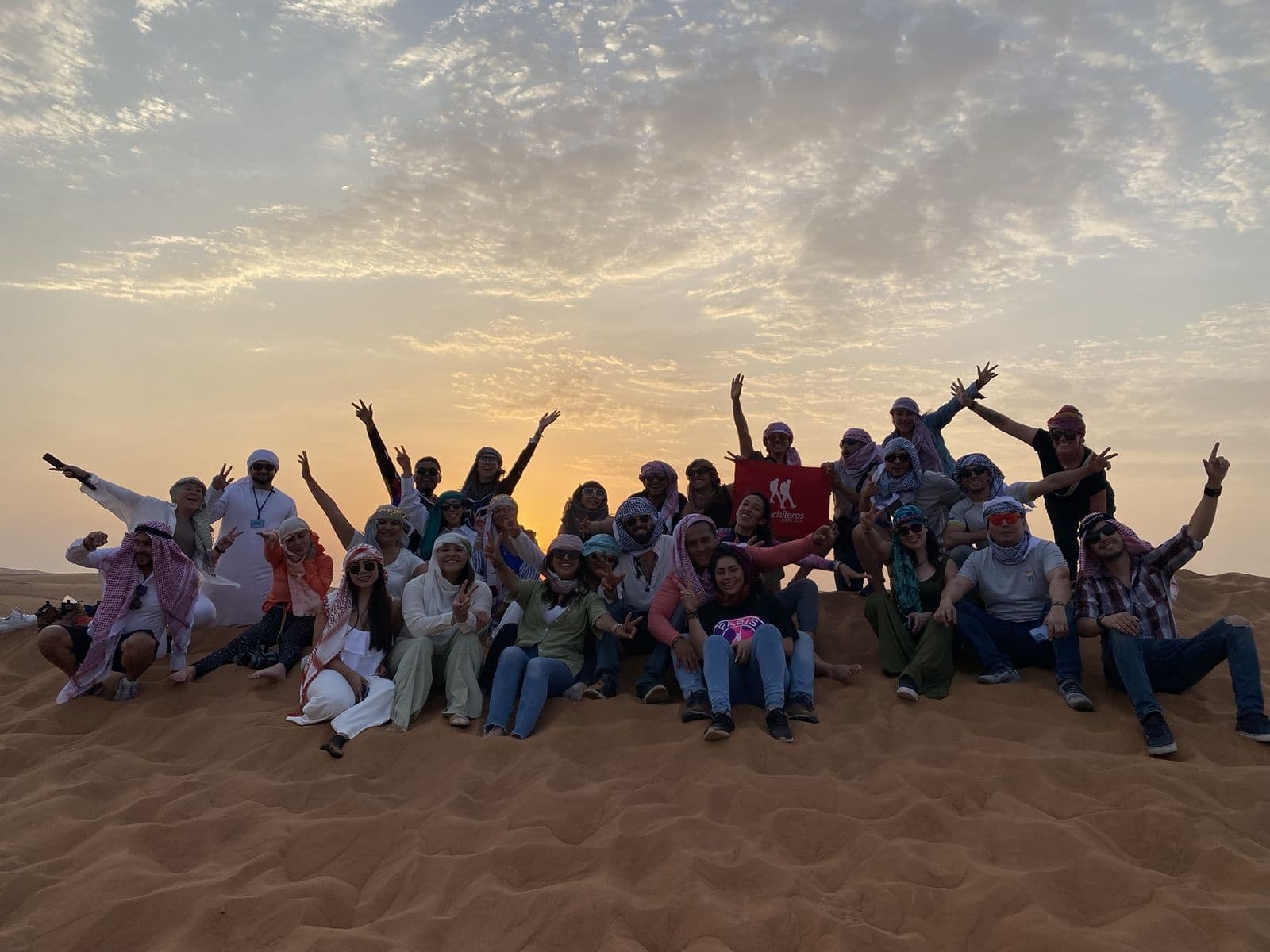 Large group of guests in headscarves celebrating together on a red dune