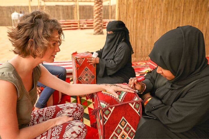 Henna artist painting a design on a guest’s hand at the evening camp