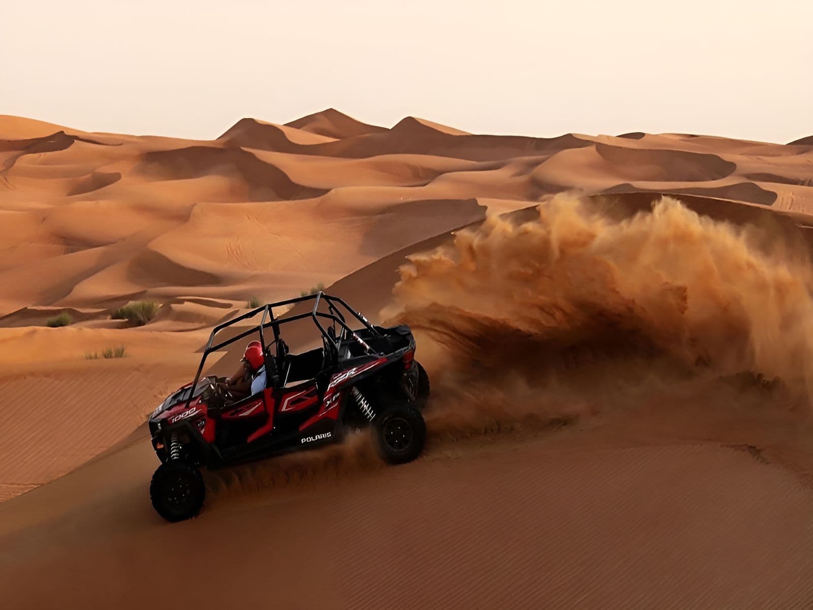 Red four-seat dune buggy driving across the red dunes