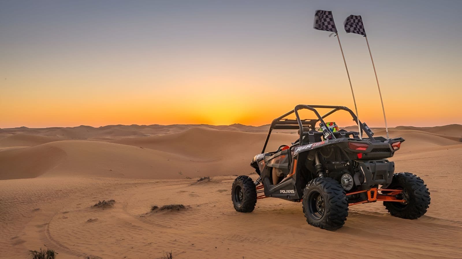 Parked dune buggy with chequered flags facing a desert sunset
