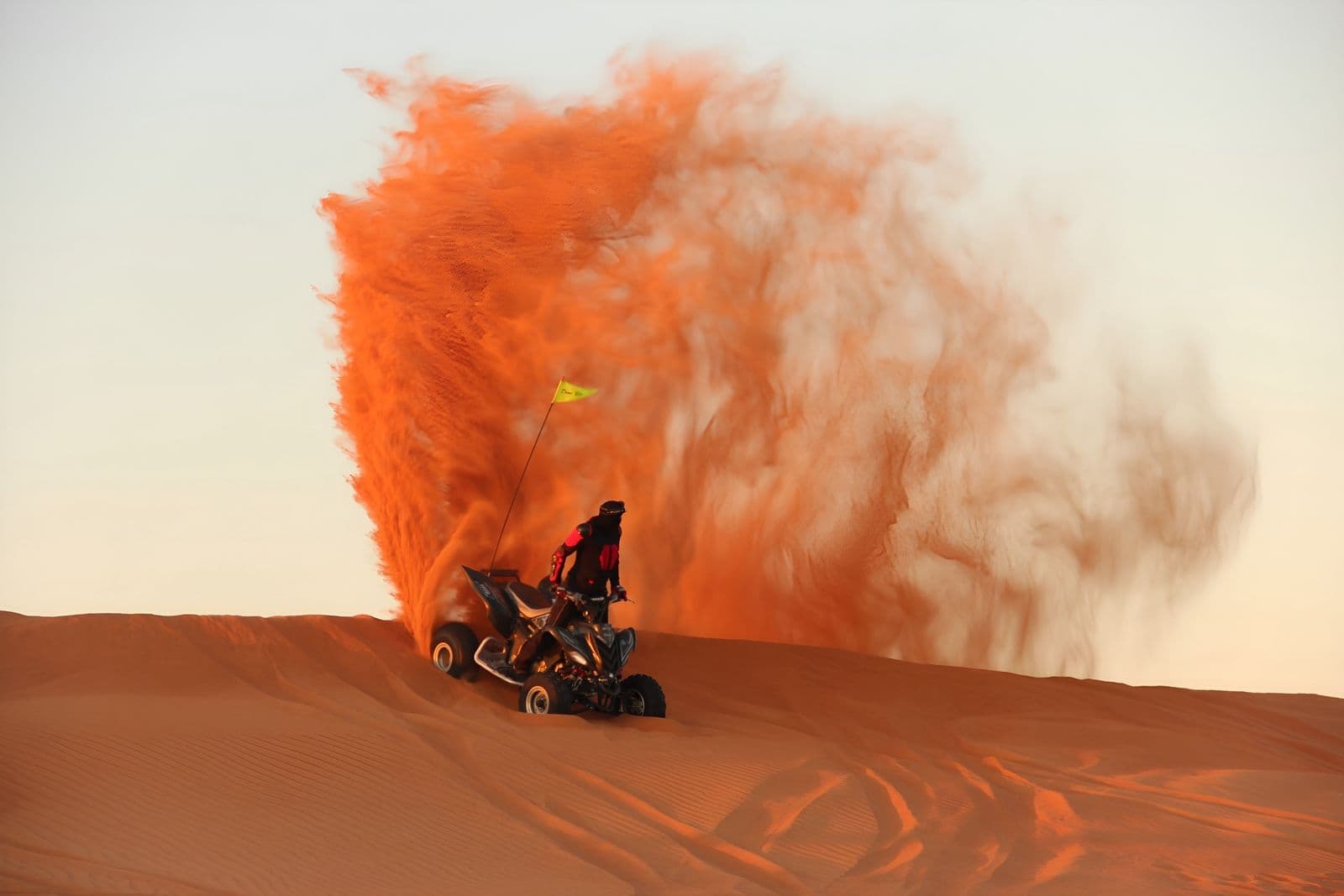 Quad bike on a dune crest with a cloud of orange sand behind it