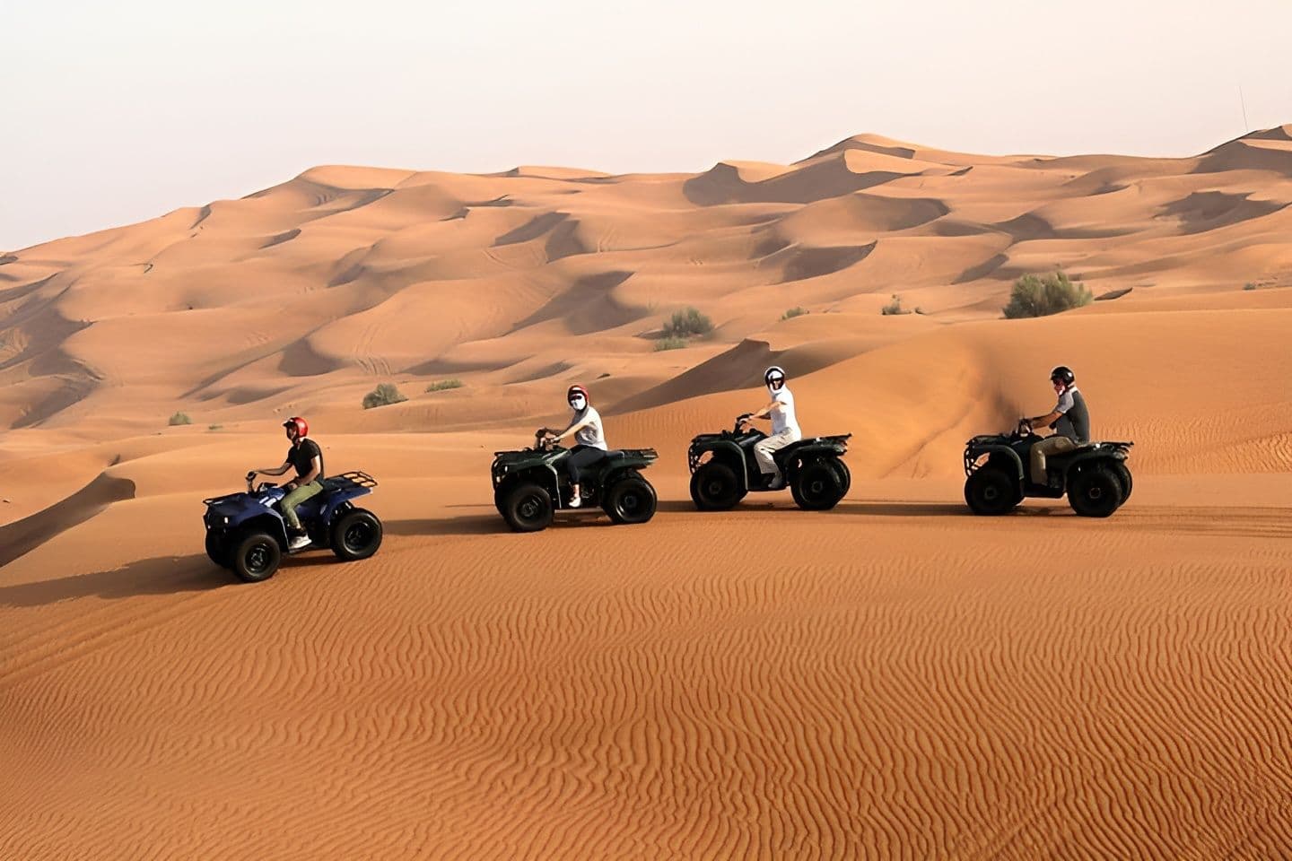 Four guests riding quad bikes in a line across the red dunes